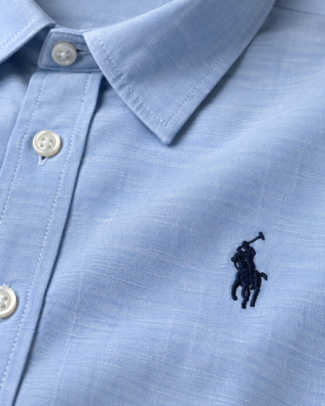 Close-up of the navy embroidered logo, collar and buttons on the baby blue shirt