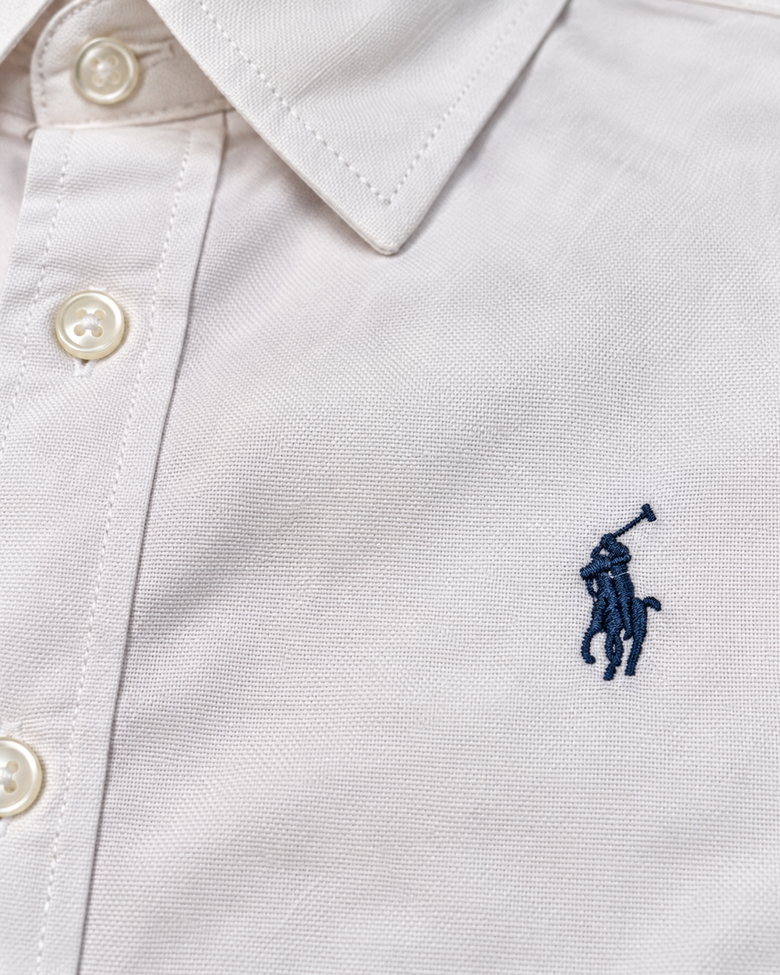 Close-up of the navy embroidered chest logo on the white Oxford shirt